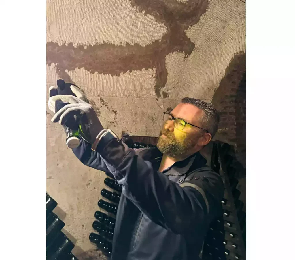 A man holds a bottle of Champagne in a horizontal position to the light in a cellar